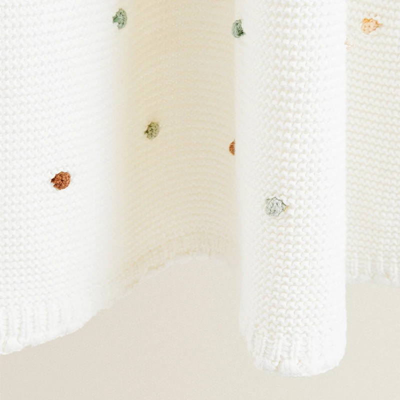 Off-white knitted fabric with small colored dots and a ribbed border.
