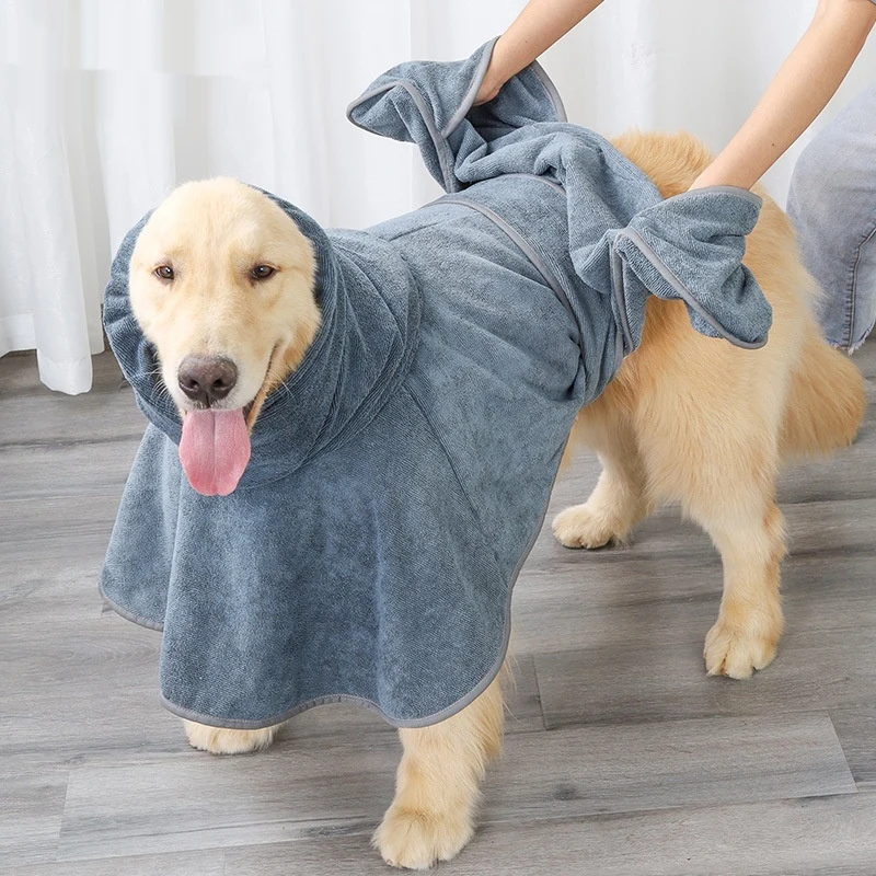 A golden retriever wearing a gray bath wrap while a person holds the towel fabric over its back.