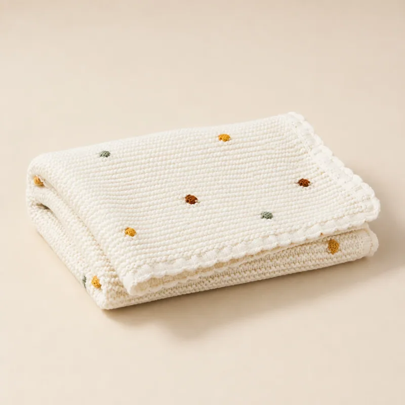 Folded off-white knitted blanket with small colored dots.